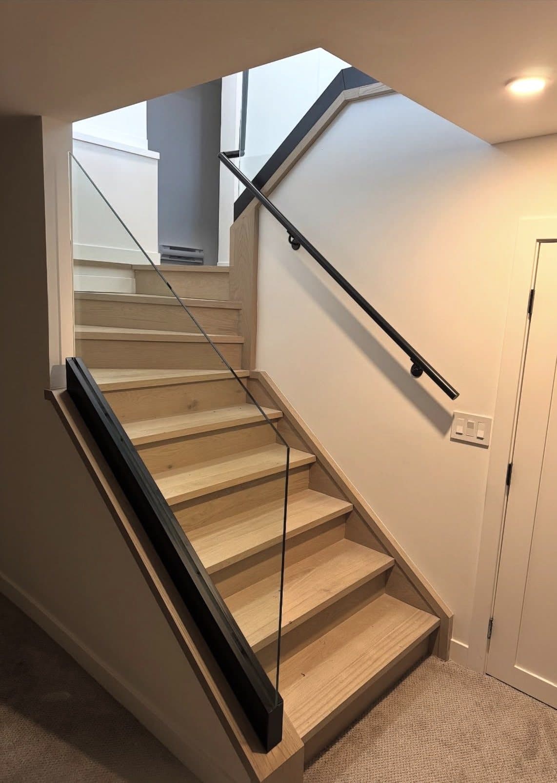 Glass stair railing with a slim handrail beside oak treads