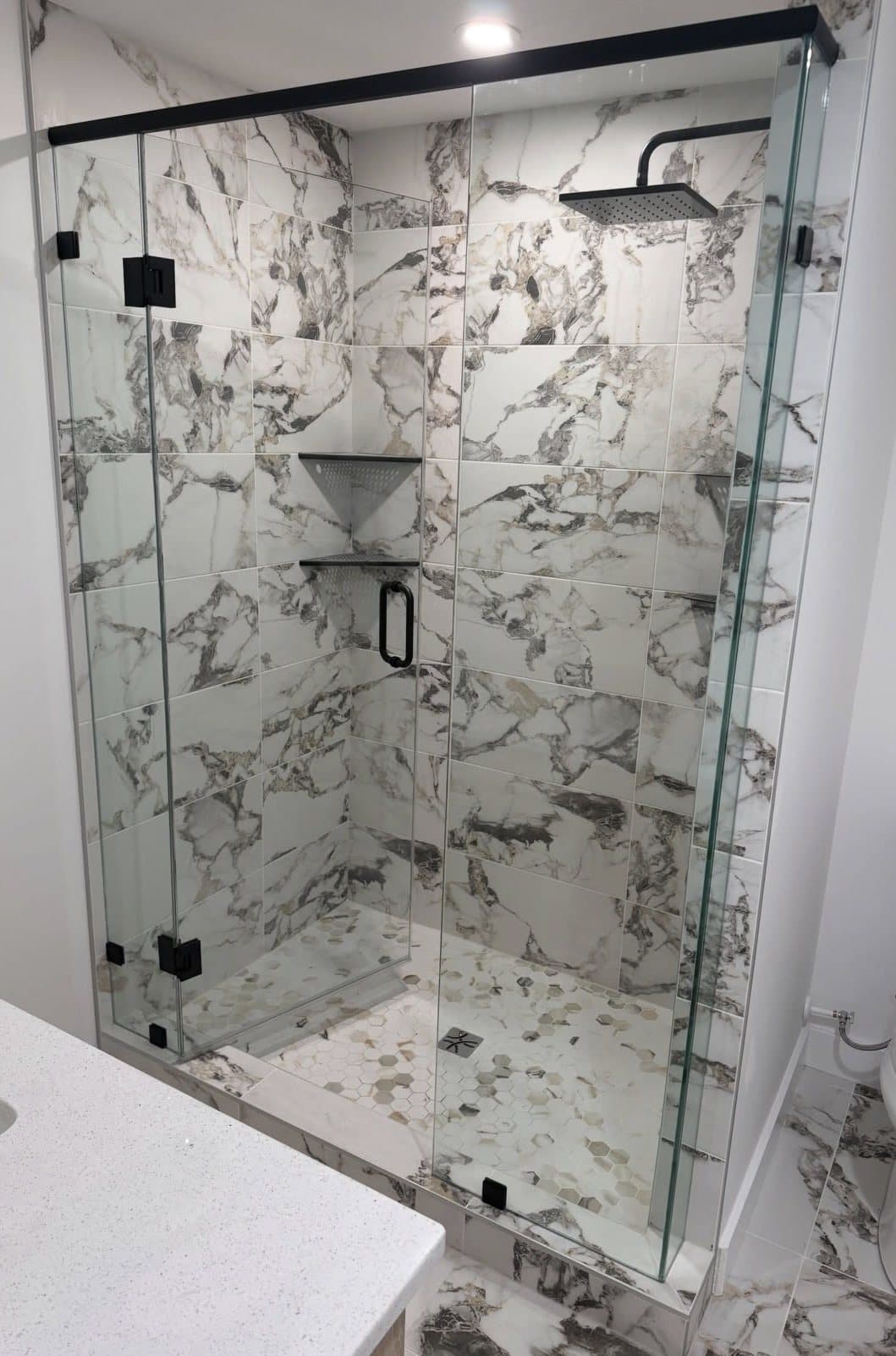 Corner shower enclosure with clear glass panels and black hardware on marble tile