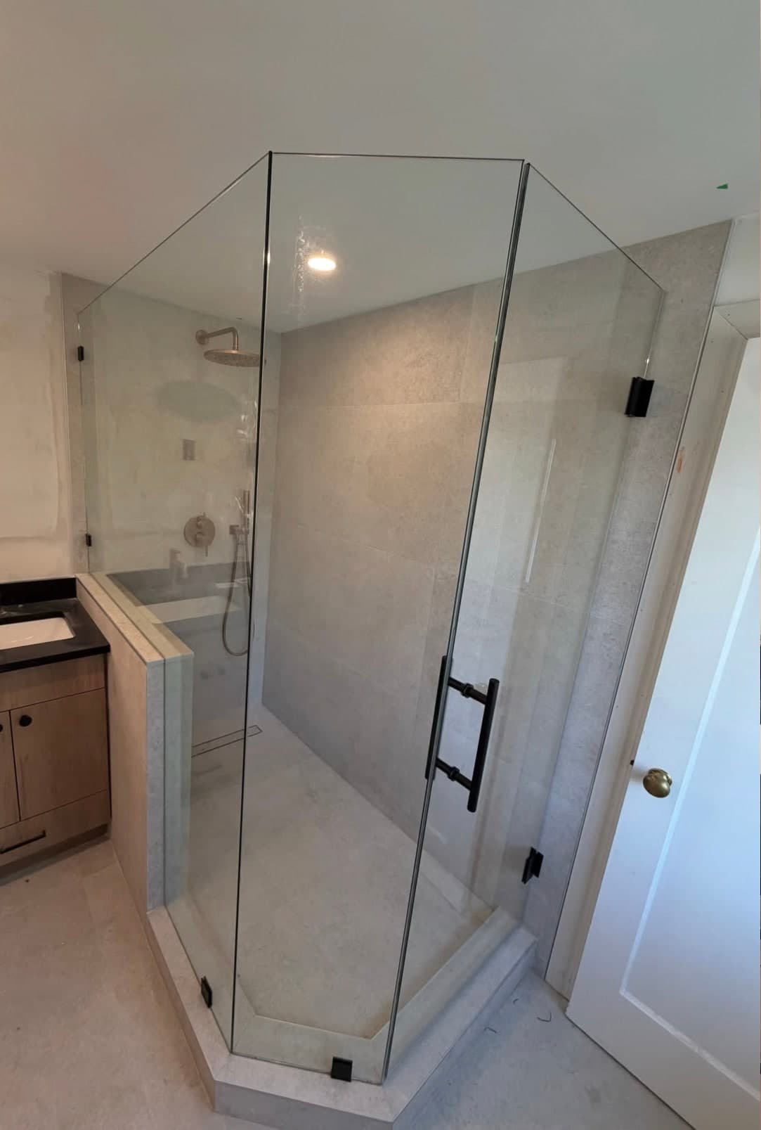 Neo-angle glass shower enclosure with a black handle in a stone-tiled bathroom