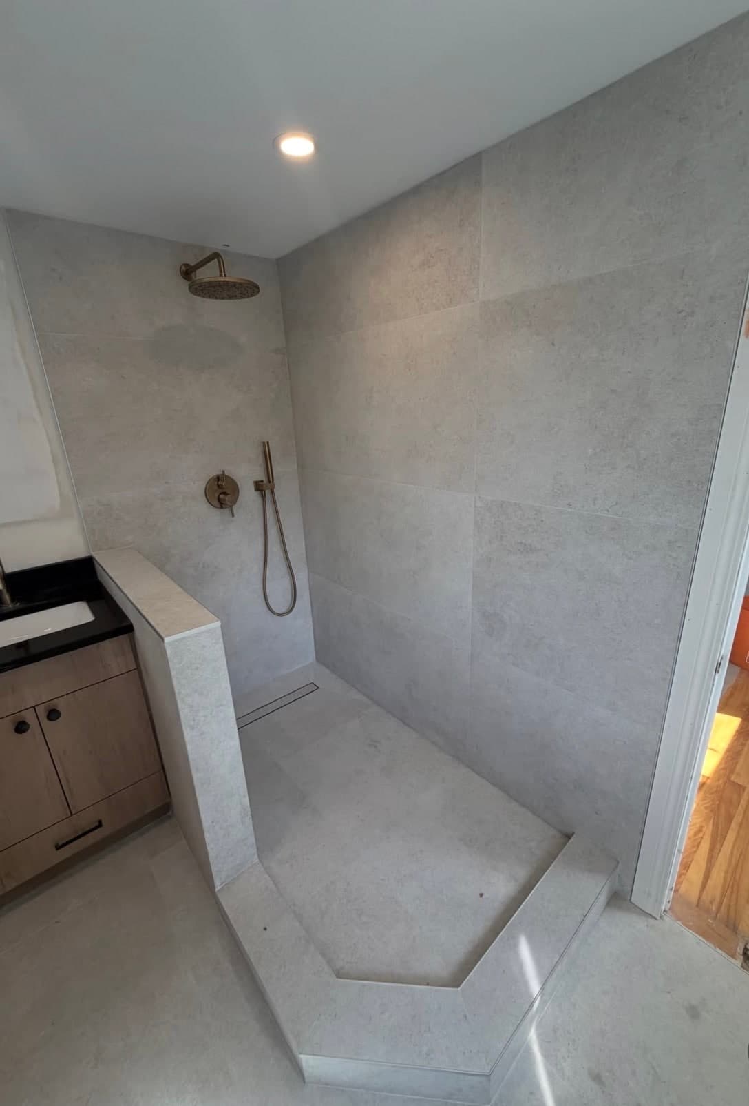 Stone-tiled shower with a brass rain head and no glass fitted